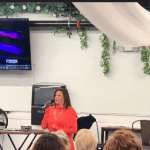 Woman speaking at a digital marketing event about transforming AI hype into practical web strategies for small businesses.